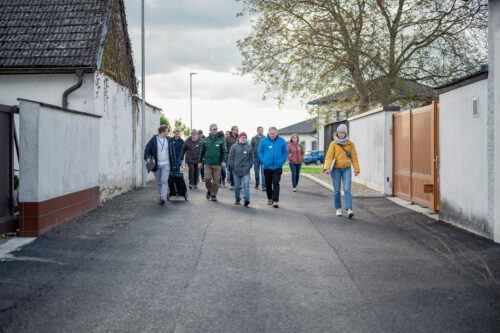 Eine Gruppe von Menschen geht eine schmale Straße entlang, die von hohen weißen Mauern flankiert wird.