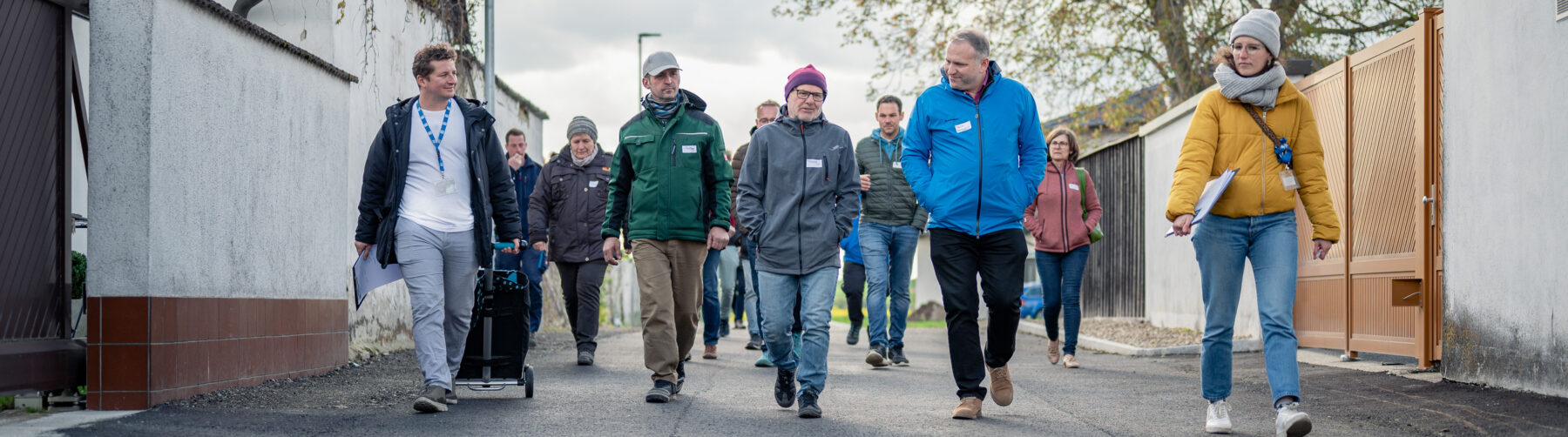 Eine Gruppe von Menschen geht eine schmale Straße entlang, die von hohen weißen Mauern flankiert wird.