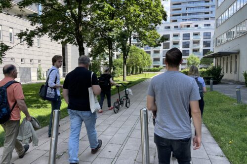 Eine Gruppe spaziert einen Weg entlang. IM Hintergrund hohe Gebäude.