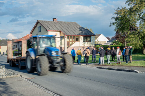 Ein blauer Traktor vor einer Menschengruppe, die sich untereinander austauscht und auf einer Wiese stehen.