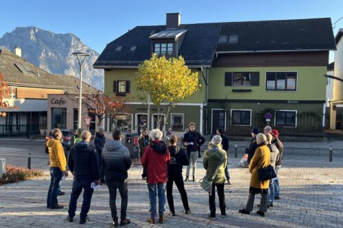 Eine Menschengruppe steht in einem Kreis auf einem Dorfplatz.