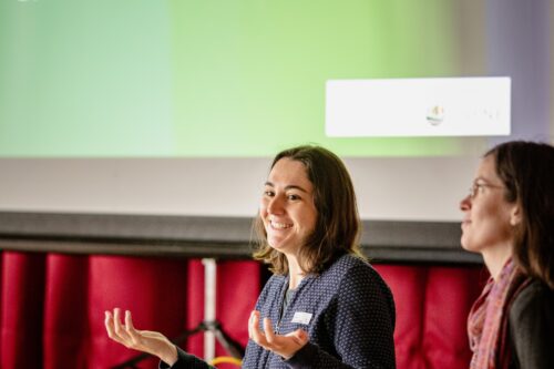 Zwei Personen sprechen vor einer Leinwand.